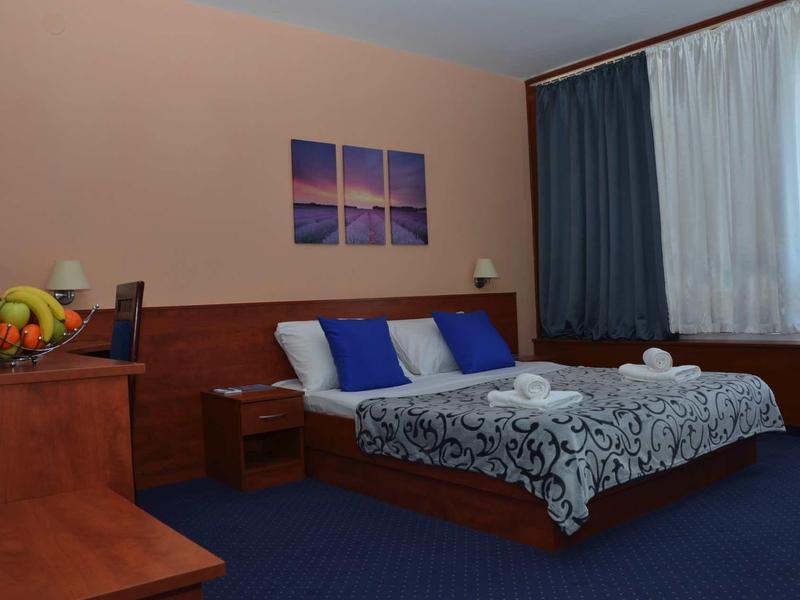 Accogliente camera d'hotel con letto matrimoniale, moquette blu e tavolo con cesta di frutta.