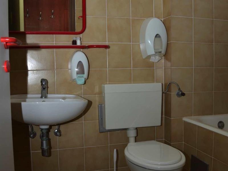 Piccolo bagno con lavandino, WC, distributore di sapone e vasca con piastrelle marroni.
