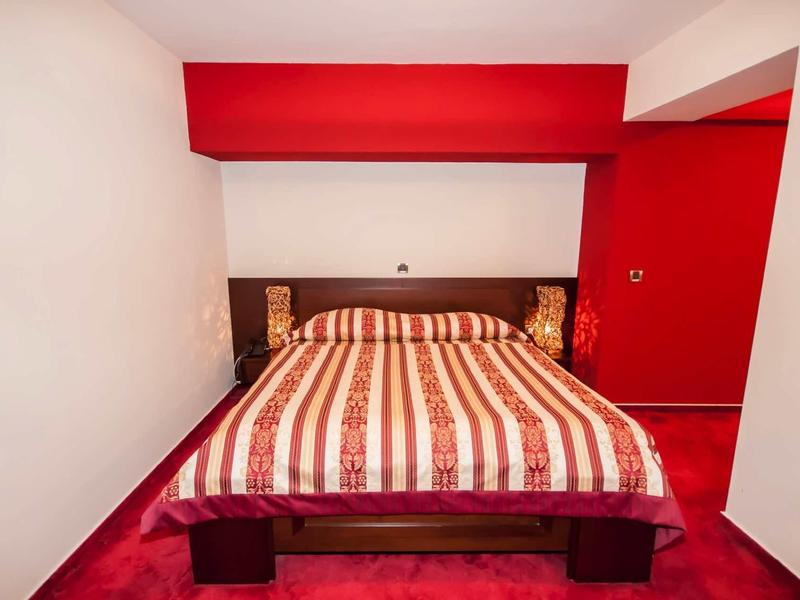 Ein schlichtes Schlafzimmer mit rotem Teppich, roter Wand, Holzbett und gestreifter Bettdecke.