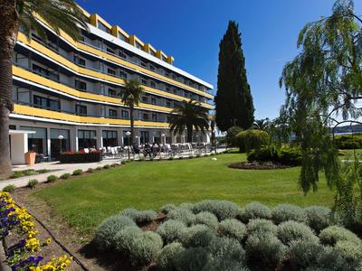 Hotelgebäude mit Balkonzimmern, gepflegtem Garten und blauen Himmel an einem sonnigen Tag.