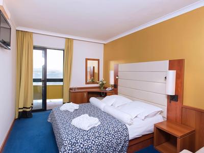 Kleines Hotelzimmer mit Doppelbett, Schreibtisch, Stuhl und Balkon mit Blick nach außen.