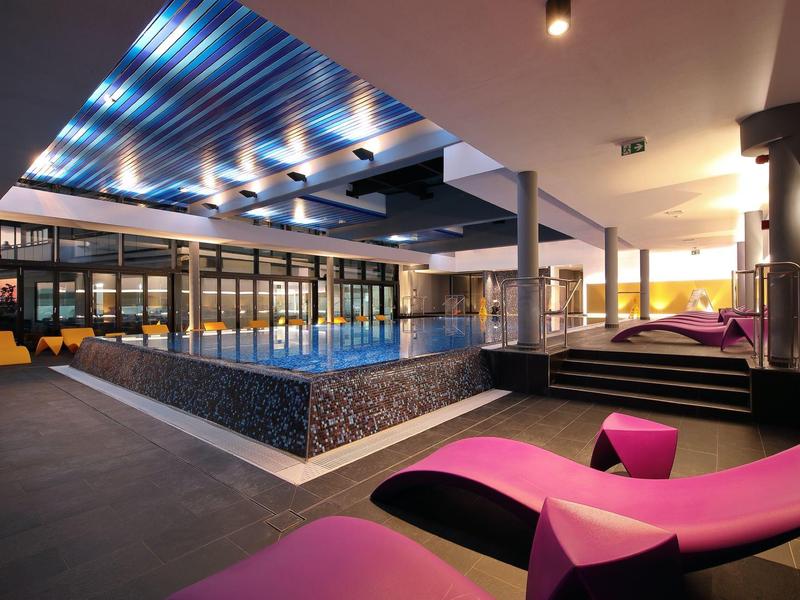 Modern hotel swimming pool with illuminated pool and colorful loungers in warm light.