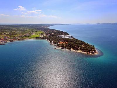 Vue aérienne d'une étroite péninsule avec mer bleue et terre boisée sous le soleil.