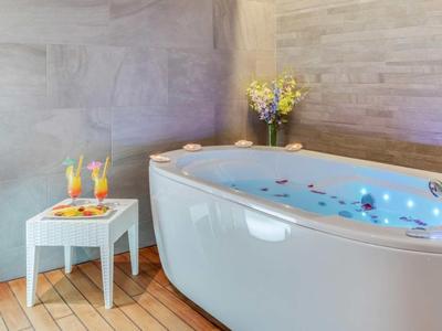 Baignoire blanche avec pétales de rose dans une salle de bains luxueuse, table avec boissons et en-cas.