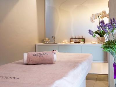 Une salle de spa lumineuse avec une table de massage, des serviettes et un bouquet de fleurs sur la table.