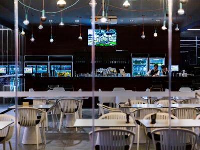 Espace bar d'hôtel moderne avec chaises, tables et comptoir éclairé sous des suspensions.