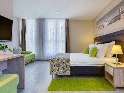 Chambre d'hôtel moderne avec sol en bois clair, grand lit et accents verts.