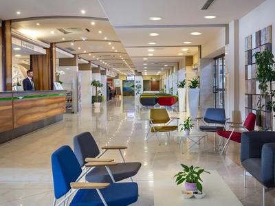 Moderner Hotel-Lobbybereich mit bequemen Stühlen, Pflanzen und Empfangstheke.