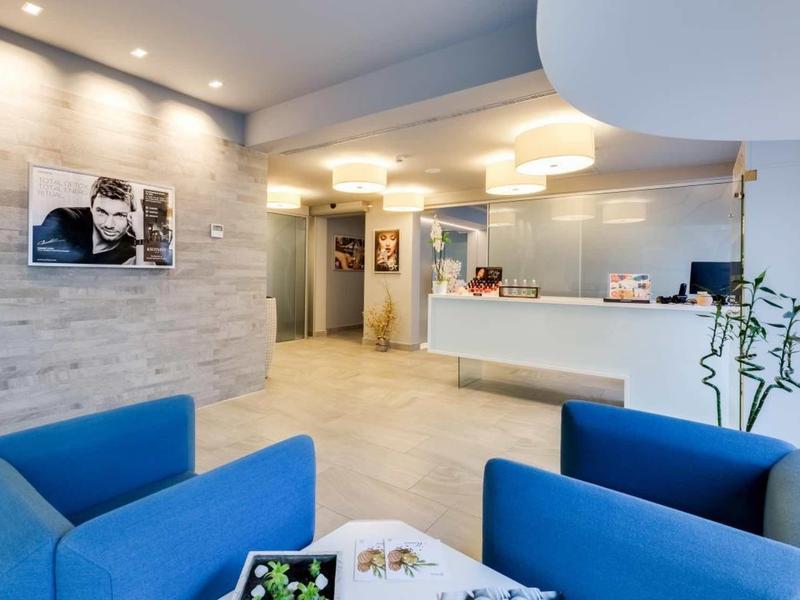 Hall d'hôtel moderne avec fauteuils bleus et comptoir d'accueil blanc sous un éclairage chaleureux.