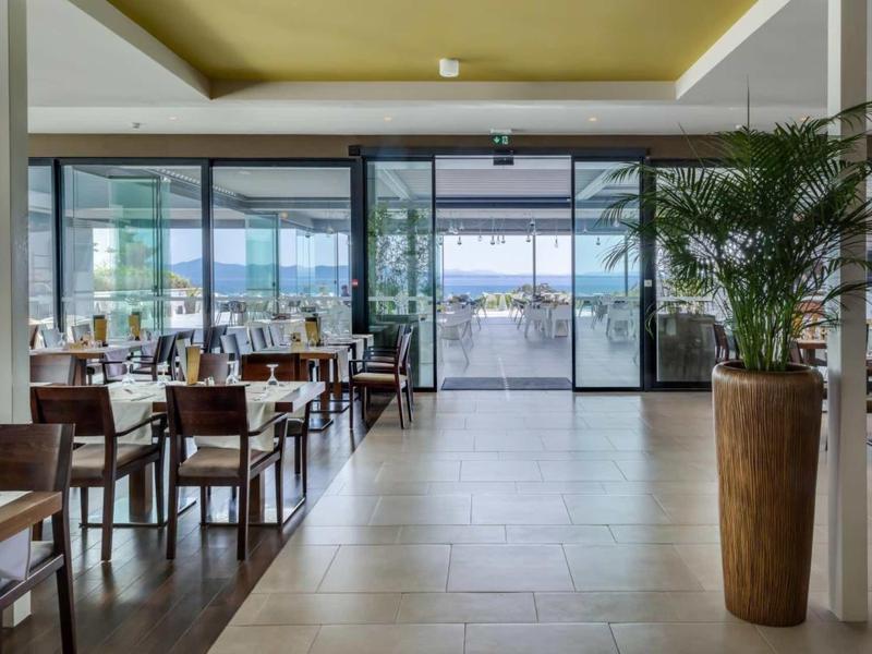 Espace lumineux du restaurant de l'hôtel avec tables, chaises et vue sur une terrasse et un paysage aquatique.