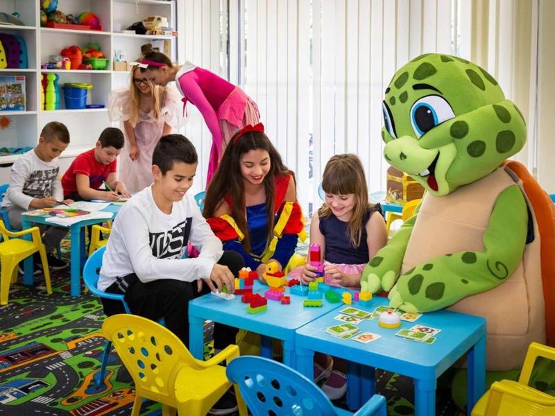 Des enfants jouent à des tables dans une salle de jeux colorée et bien équipée avec des encadrants.