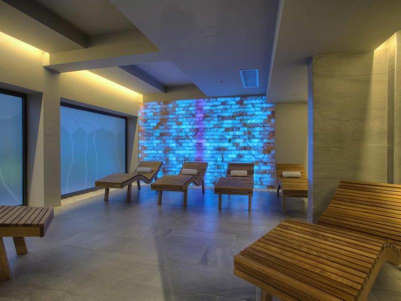 Espace lounge avec mobilier en bois rayé et mur en pierre éclairé en bleu.