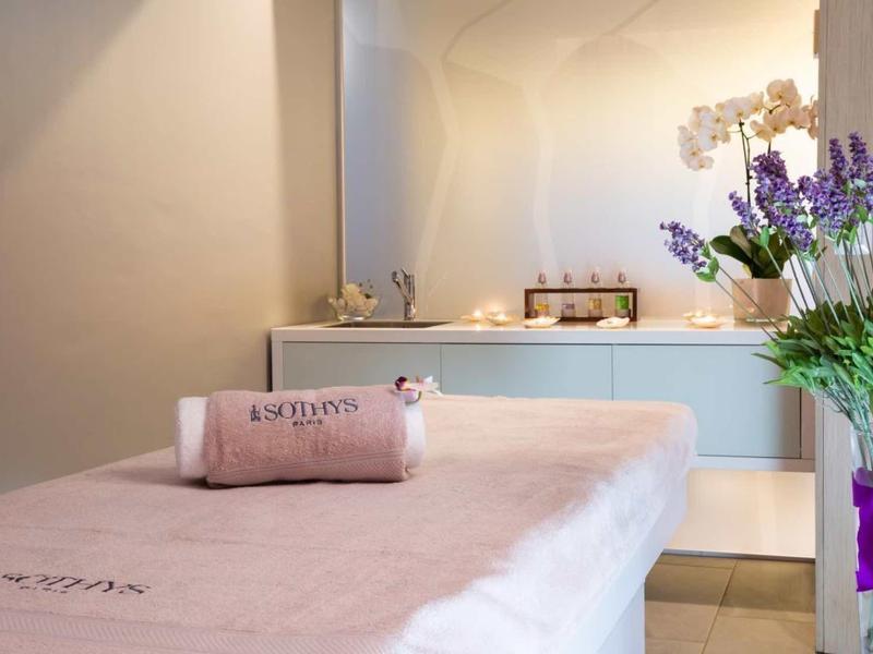 Une salle de spa lumineuse avec une table de massage, des serviettes et un bouquet de fleurs sur la table.
