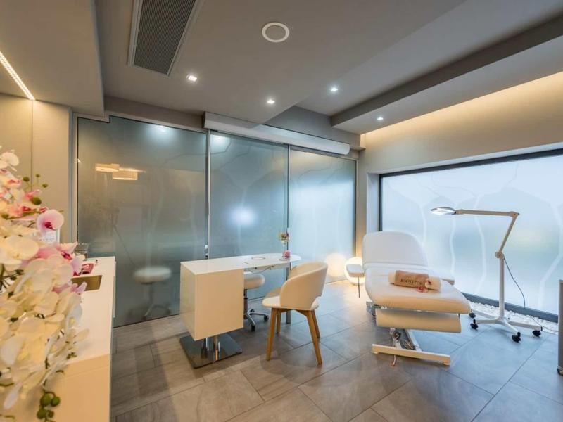 Salle de soin lumineuse avec fauteuil inclinable, chaises et mur en verre dans un spa hôtelier.