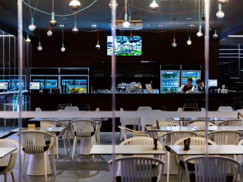 Espace bar d'hôtel moderne avec chaises, tables et comptoir éclairé sous des suspensions.