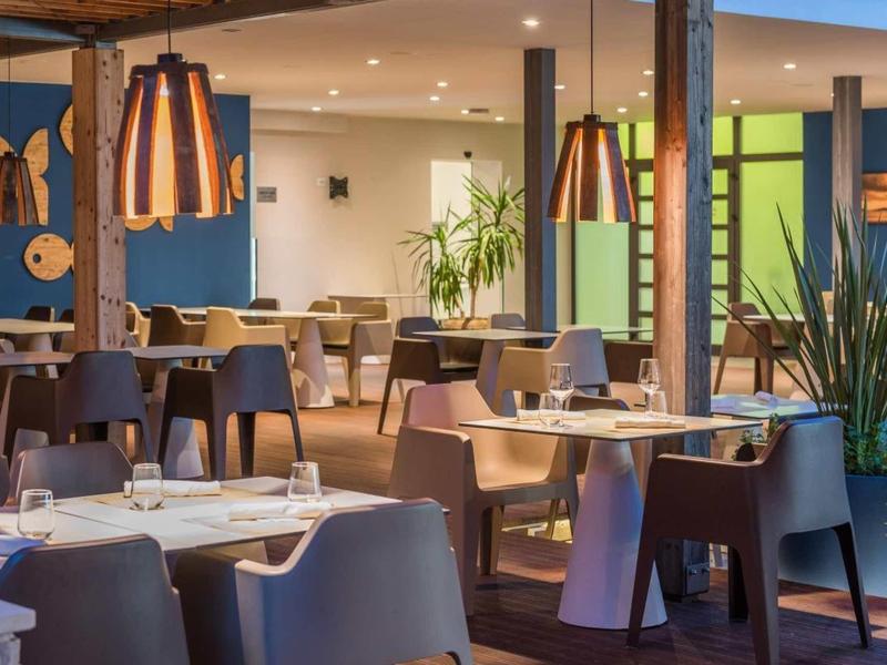 Espace repas d'hôtel moderne avec des tables élégantes, des chaises et un éclairage décoratif.