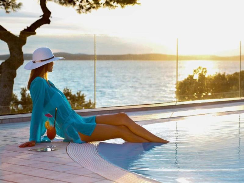Femme détendue au bord de la piscine avec vue sur la mer au coucher du soleil.