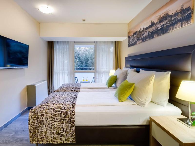 Chambre d'hôtel moderne avec deux lits, porte-fenêtre et éclairage chaleureux.