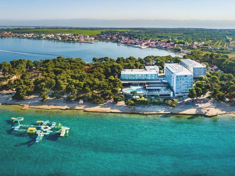 Hôtel côtier avec plage de sable et eau bleue claire, entouré d'arbres.