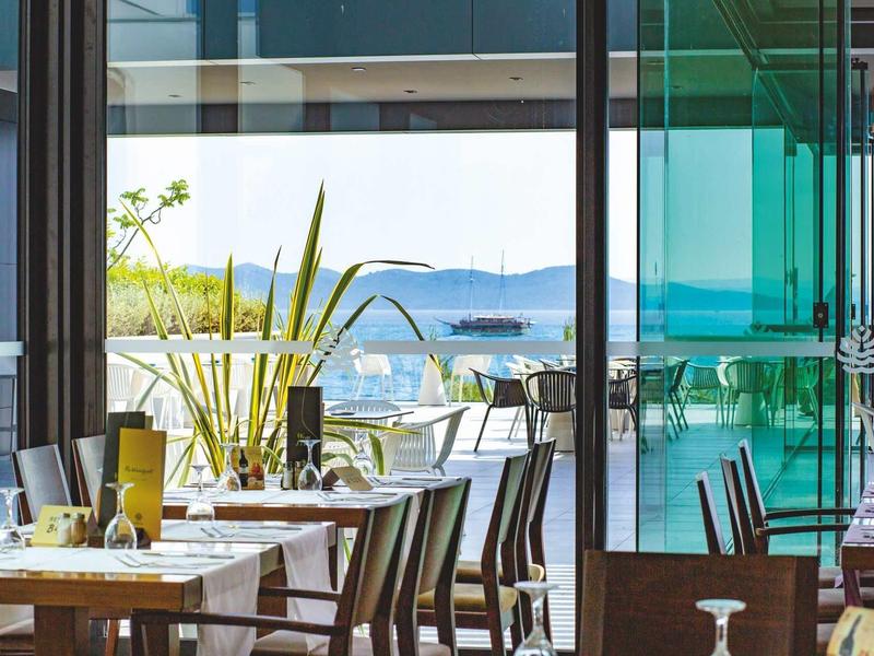Restaurant moderne avec chaises en bois et vue sur la mer, terrasse extérieure ensoleillée.