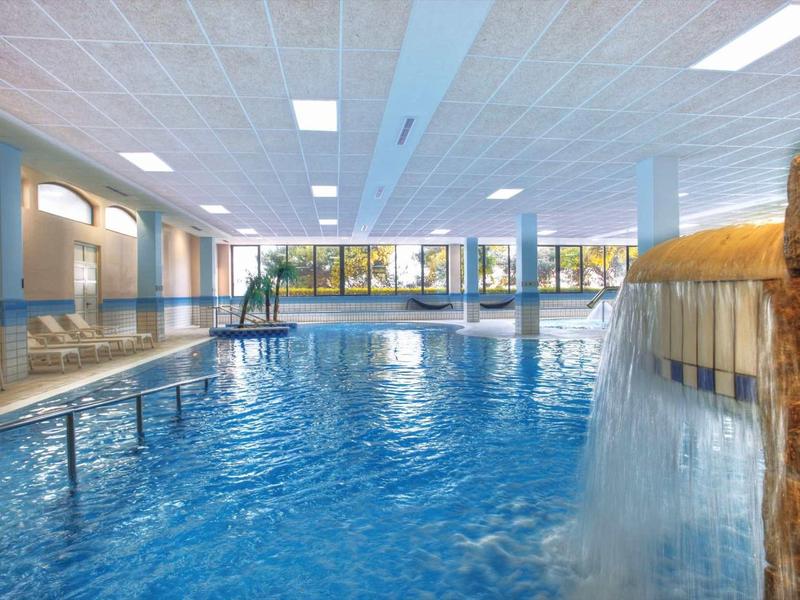Piscine intérieure avec cascade et grandes fenêtres laissant entrer la lumière du jour.