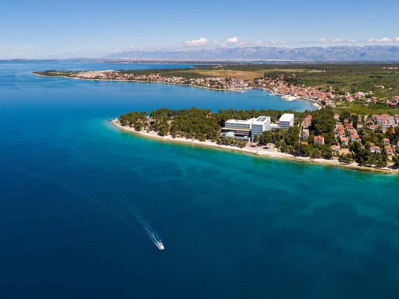 Littoral avec mer bleue, plage, hôtels et un bateau sur l'eau sous un ciel clair.