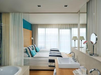 Nowoczesny pokój hotelowy z podwójnym łóżkiem, dużym oknem oraz łazienką z umywalką i wanną.