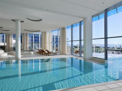 Jasny nowoczesny basen kryty z dużymi oknami i widokiem na morze.