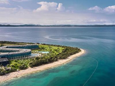 Luftaufnahme eines Resorts mit Pool an einer Küste mit klarem, blauem Wasser und Sandstrand.