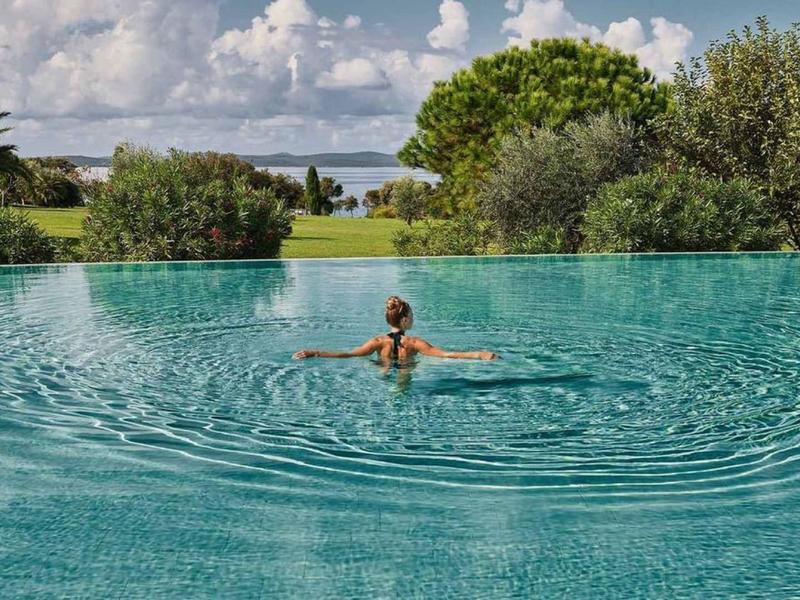 Osoba relaksuje się w basenie infinity z widokiem na drzewa i pochmurne niebo.