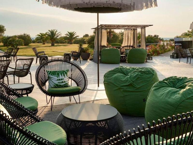 Przytulne miejsca do siedzenia z zielonymi poduszkami i parasolami na hotelowym tarasie o zachodzie słońca.