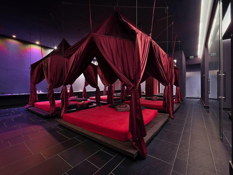Wnętrze z ciemnoczerwonymi, wyściełanymi miejscami do siedzenia pod tkaninowymi daszkami w nowoczesnym otoczeniu.