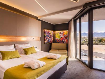 Modern hotel room with double bed, sofa, artwork, and large balcony with mountain view