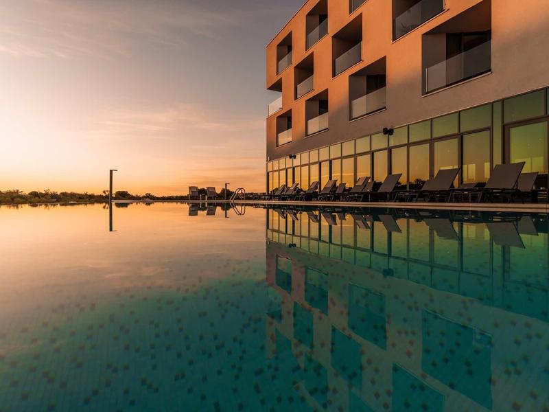 Modern hotelzwembad bij zonsondergang met reflectie van het gebouw in het water.