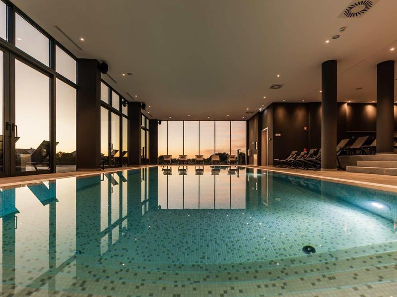 Binnenruimte van een hotel met groot verlicht zwembad en zitgedeelte bij zonsondergang.