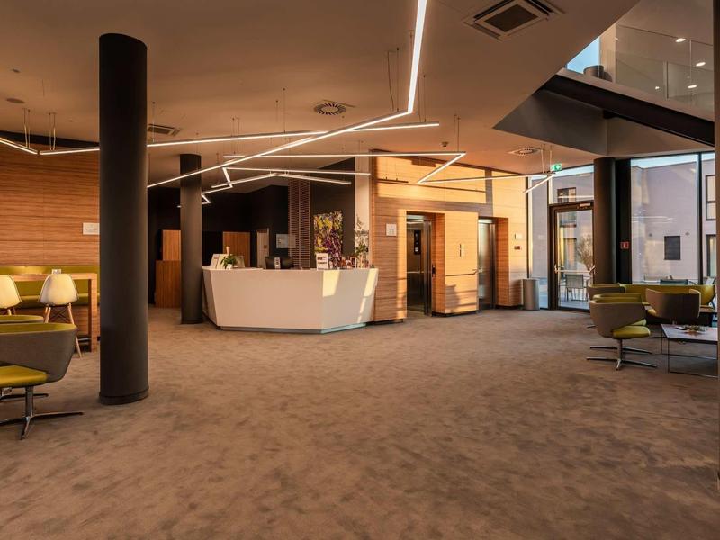 Ruime hotellobby met receptiebalie, moderne zitplaatsen en tapijtvloer.
