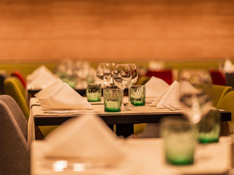 Elegant restaurant met gedekte tafels, witte servetten en groene waterglazen.