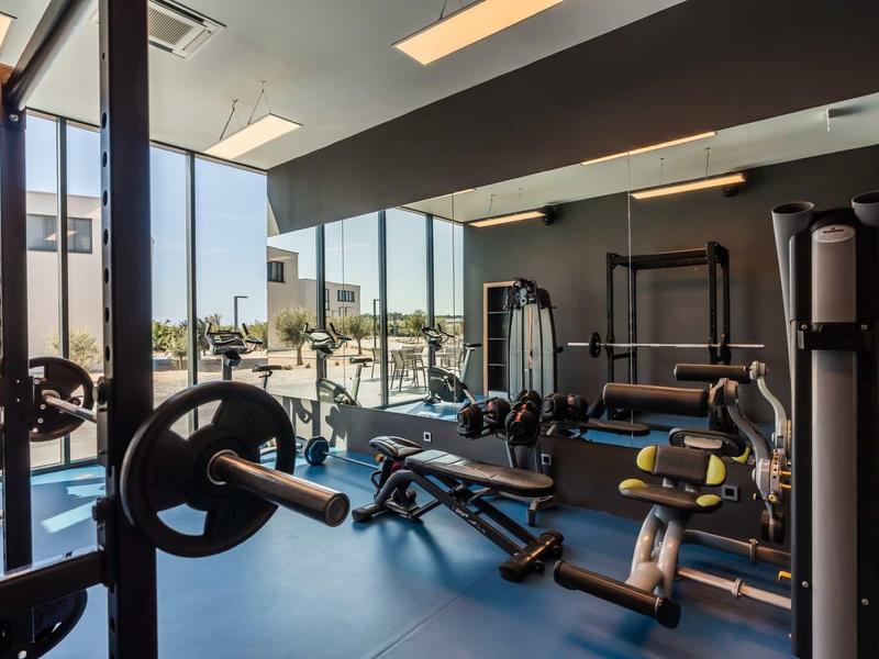 Moderne fitnessruimte met halters, fitnessapparatuur en grote ramen met uitzicht naar buiten.