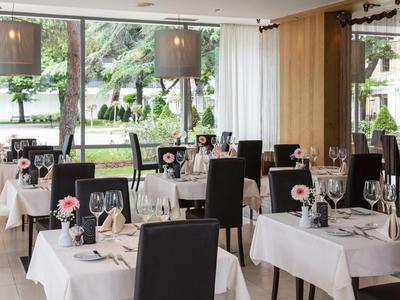 Modern restaurant met witte tafelkleden, zwarte stoelen en uitzicht op de tuin.