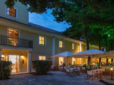 Avondexterieur van een hotel met verlichte restaurantgedeelte en tafels onder parasols