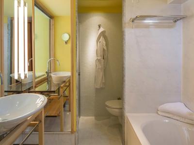 Lichte badkamer met wastafel, douche, bad en badjas aan de muur.