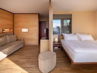 Camera d'hotel arredata in stile moderno con letto matrimoniale, divano, pavimento in legno e balcone.