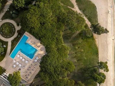Vista aerea di un hotel con piscina, area forestale adiacente e spiaggia sul mare.