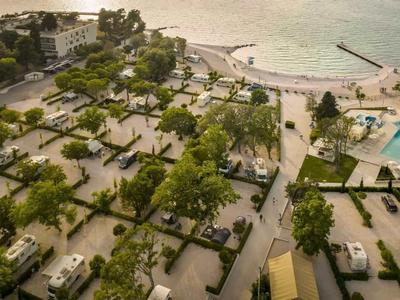 Vista aerea di un resort sulla spiaggia con ville, alberi e una grande piscina accanto al mare.