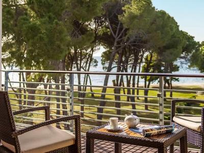 Balcone con sedie e tavolo, vista su alberi e mare sullo sfondo.