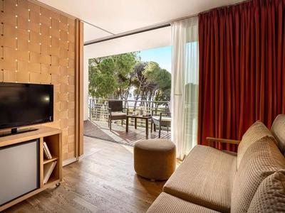 Zona accogliente della camera d'hotel con divano, TV e accesso a una terrazza con tavolo e sedie.