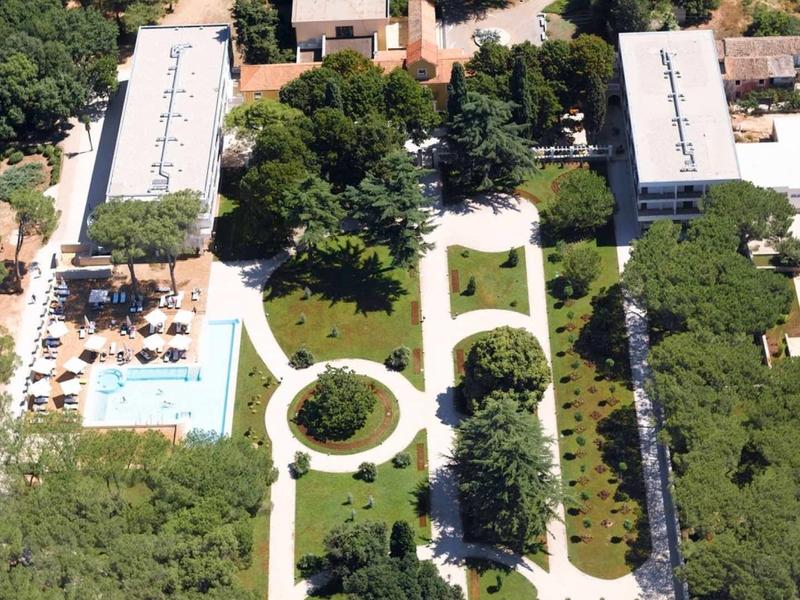 Vista aerea di un hotel con piscina, giardini e più edifici circondati da alberi.