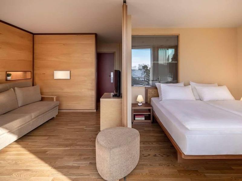 Camera d'hotel arredata in stile moderno con letto matrimoniale, divano, pavimento in legno e balcone.
