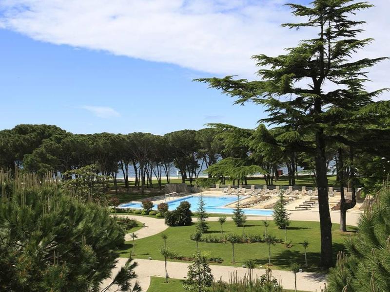 Vista di un'area piscina con sdraio e alberi sotto un cielo azzurro.