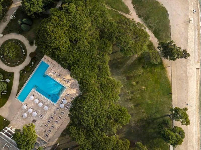 Vista aerea di un hotel con piscina, area forestale adiacente e spiaggia sul mare.